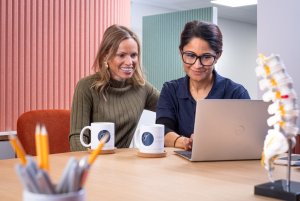 Kay shares information with Maria on a laptop